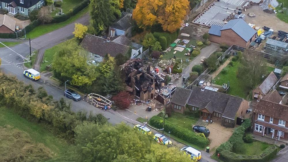 A drone shot of the street shows the ruins of an exploded house. Surrounding houses are undamaged, but the property in the centre is completely destroyed with singed bricks.