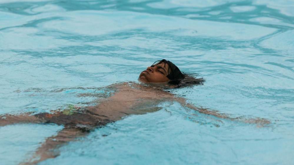Young boy floats in a blue-watered pool