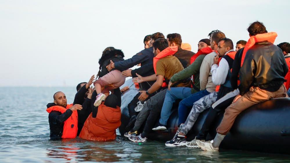 Migrants carry a young girl onboard an inflatable dinghy boat to cross the English Channel.