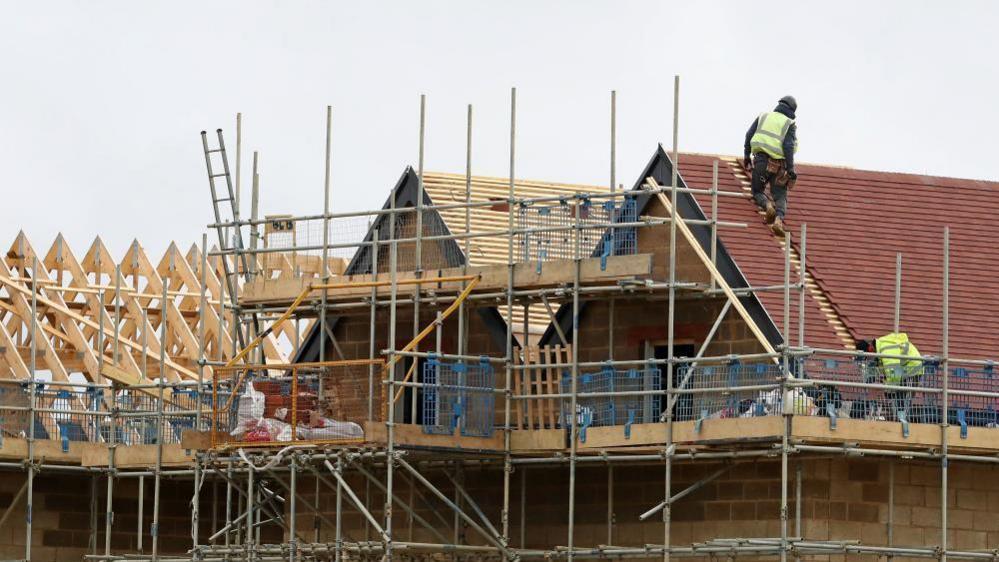 A construction worker is seen working on the roof of a house