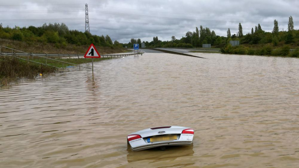 The open boot of a car is visible above the water where the vehicle is submerged in flood water on a421 in Marston Moretaine