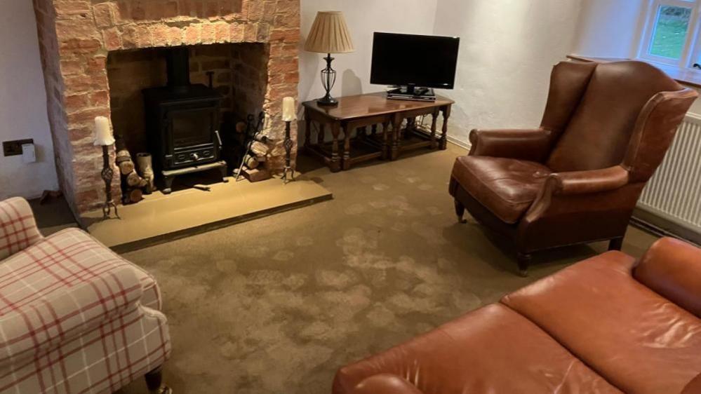 Lounge with brown armchair and sofa, beige armchair, and stone fireplace. There are patches of water on the floor.