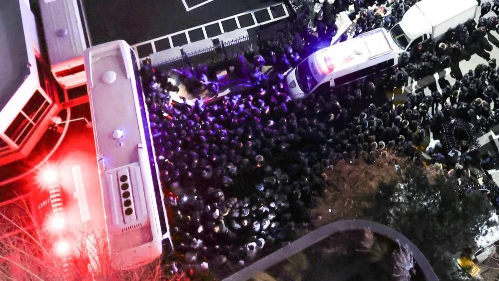 Police officers and CIO investigators gather in front of the entrance to the official residence of impeached South Korean President Yoon Suk Yeol