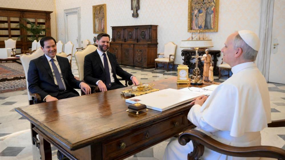 Rubio and Vance smile as they sit behind a desk facing the Pope