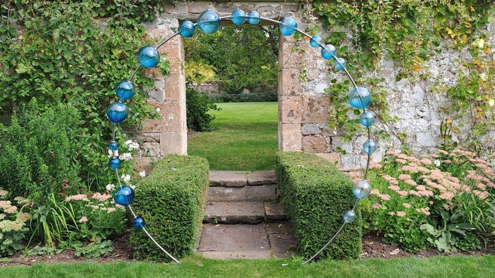 An archway over a garden path with large blue glass baubles all the way round it