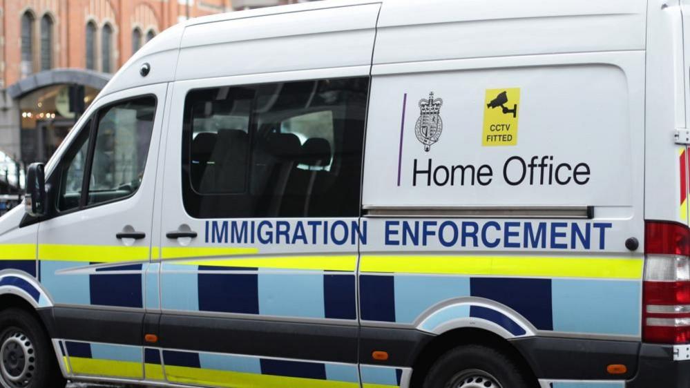 A white van with the words Home Office Immigration Enforcement is parked on a street. 