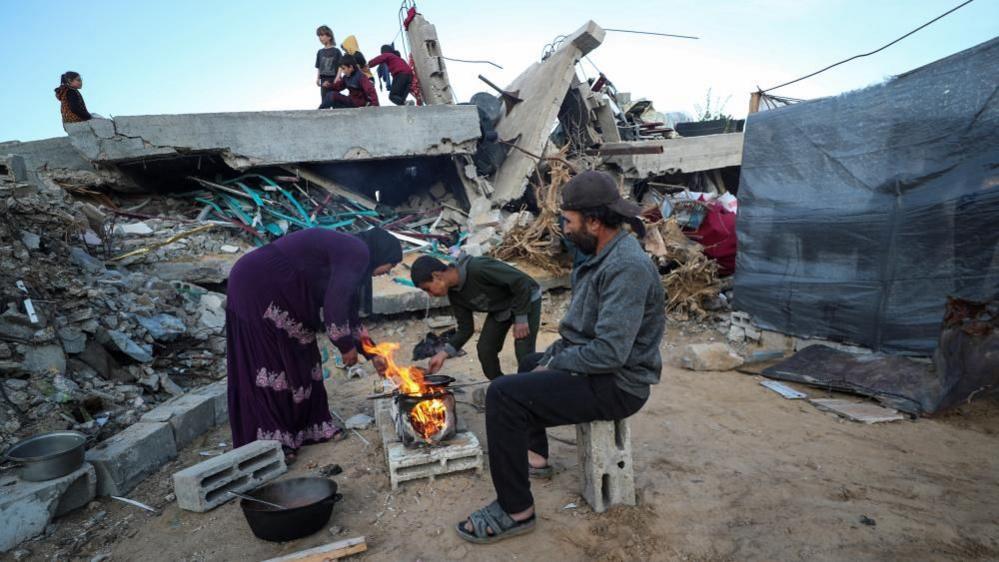 A Palestinian family prepare a meal over on open fire among destroyed buildings in Jabalia refugee camp in the northern Gaza Strip. Photo: 2 March 2025