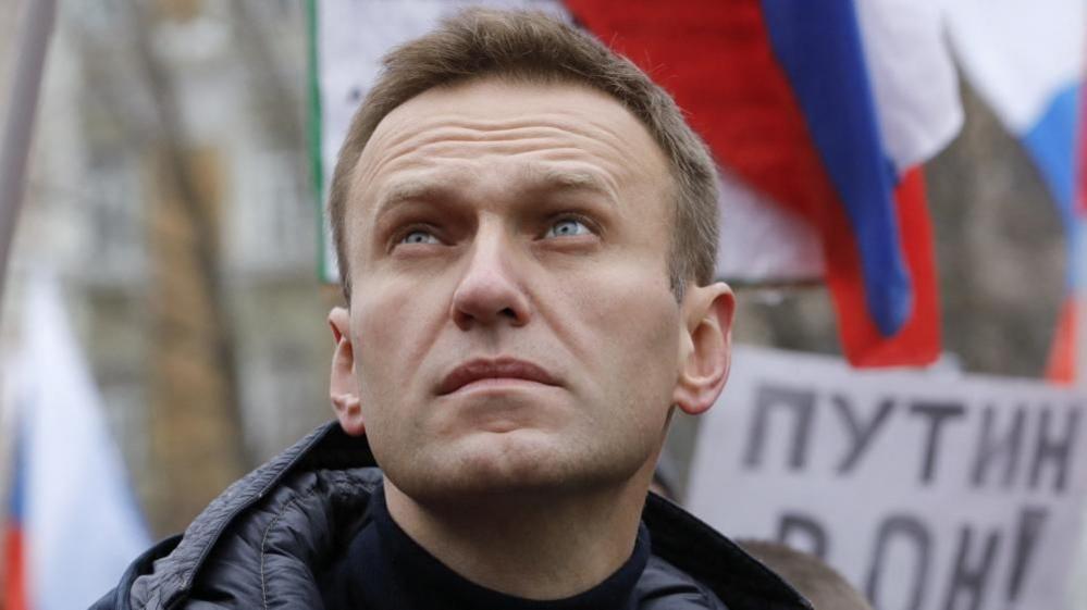 Alexei Navalny looks up as he attends a rally, as a Russian flag flutters in the background