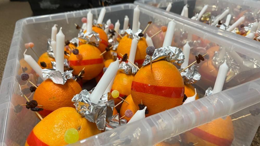 Oranges in a plastic box, with candles and fruit on cocktail sticks, ready to be used at a church service on Christmas Eve.