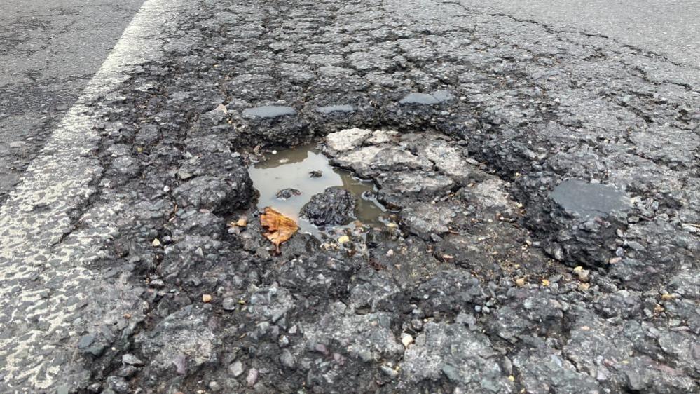 A leaf lying next to a water-filled pothole on a road in Cambridge.