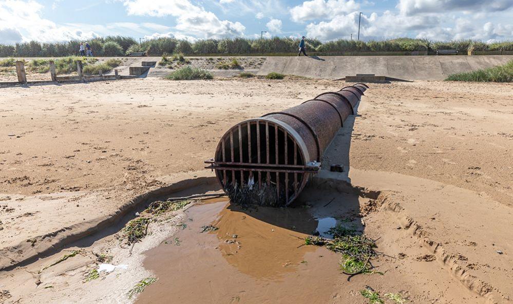 Overflow pipe outlet at the high tide level on an English coastal sand beach in Yorkshire