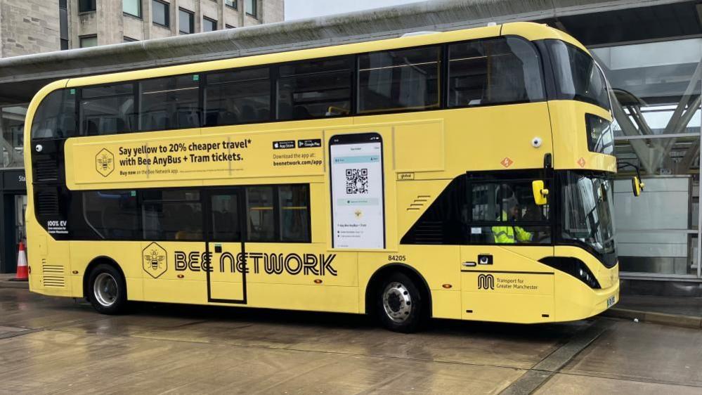 A yellow double-decker bus at a bus stop which reads 'Bee Network' on the side. 