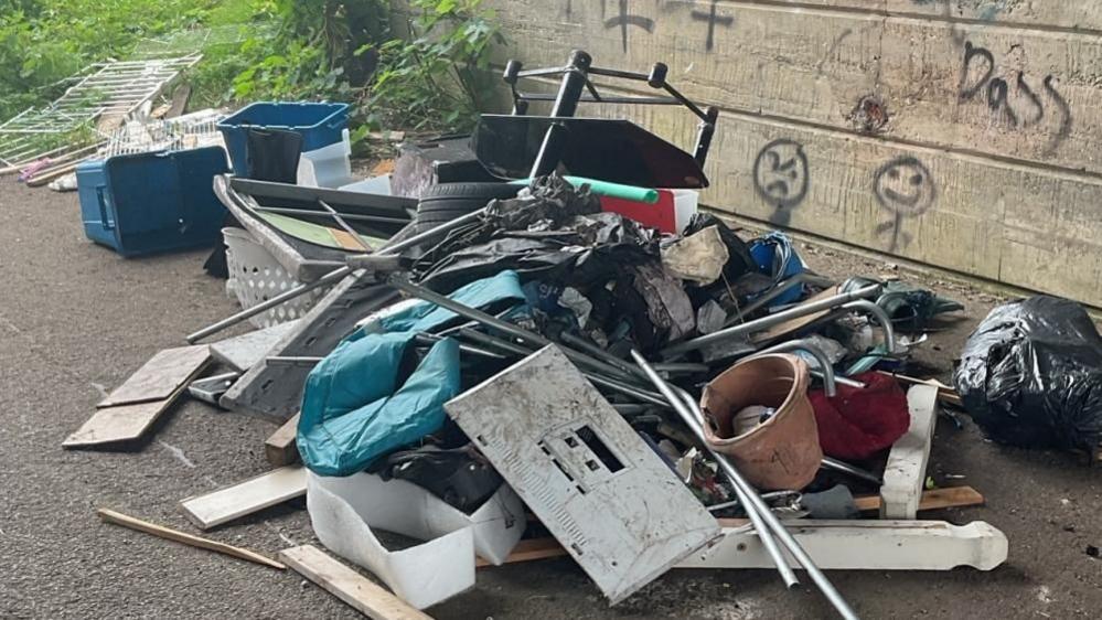 Fly-tipped waste dumped under Barnard Bridge in Great Yarmouth. Items include an old TV stand, plant pots, bed posts, metal poles and plastic boxes.