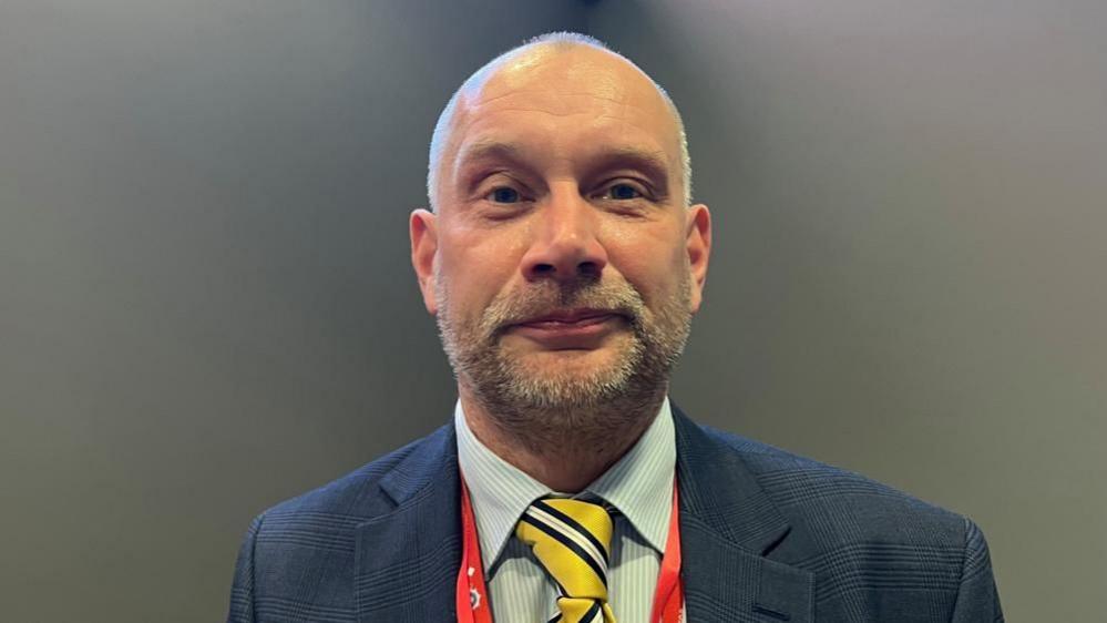 Det Insp Andy Blaize wearing suit, tie and lanyard