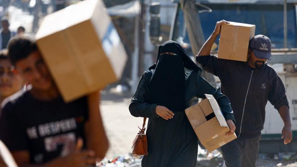 Palestinians carry aid supplies that entered Gaza, amid a ceasefire between Israel and Hamas in Gaza, in Zawaida