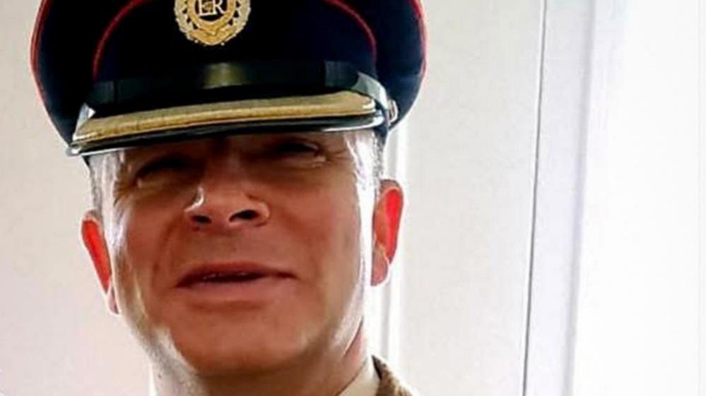 A headshot of retired Lt Col Andrew Davies in uniform. He has short hair and is wearing a military hat with an emblem with ER in its centre.