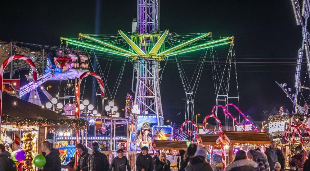 A general view of people walking through a Christmas themed fun fair at night in with a reindeer sledge ride and large red and white candy canes.