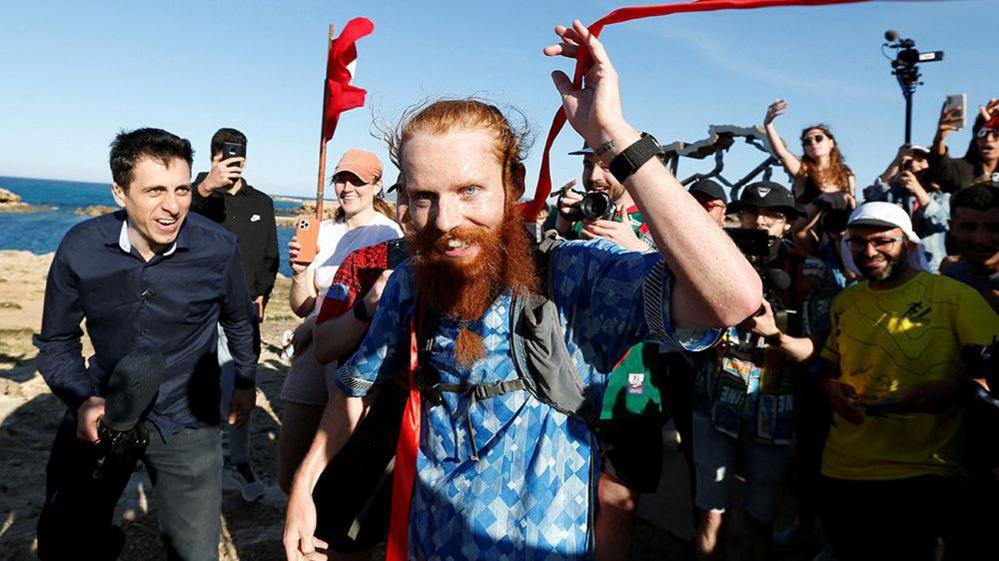 Russell Cook gestures and smiles while crossing the finishing line of his Africa run on 7 April