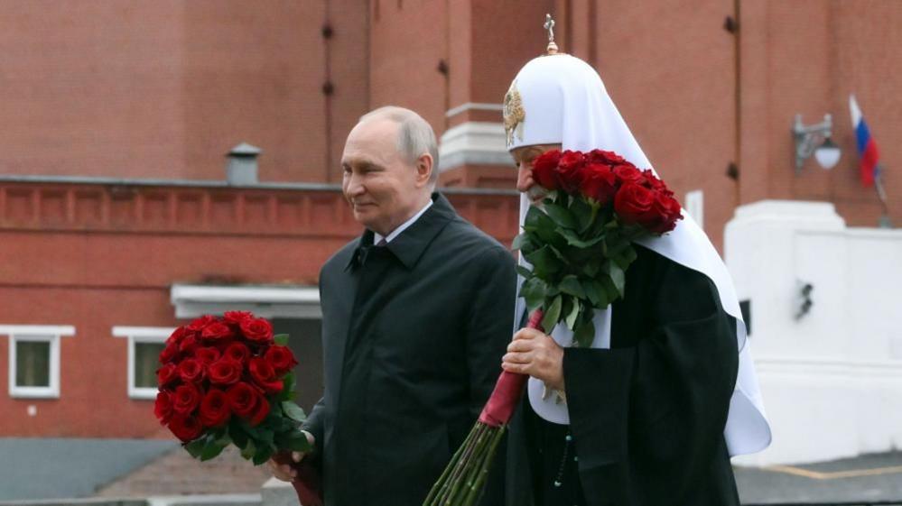 Russian President Vladimir Putin (L) and Patriarch Kirill of Moscow and All Russia take part in a flower-laying ceremony