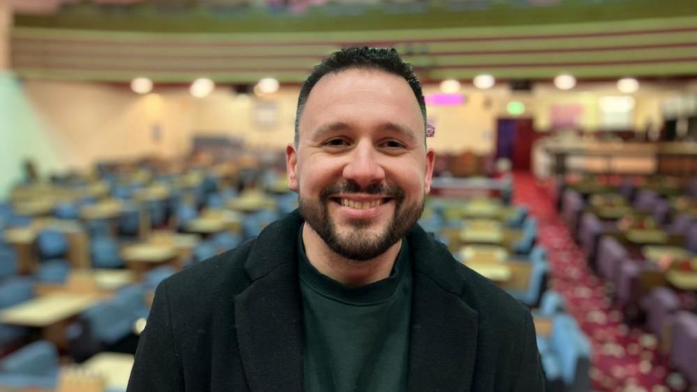 Oliver Mcloughlin standing in the bingo hall smiling and looking at the camera.