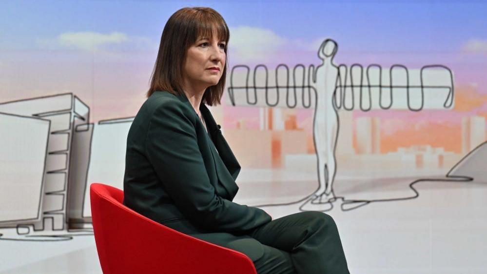 Reeves sits in the red chair on the Laura Kuenssberg, wearing a green suit, looking to the right of frame