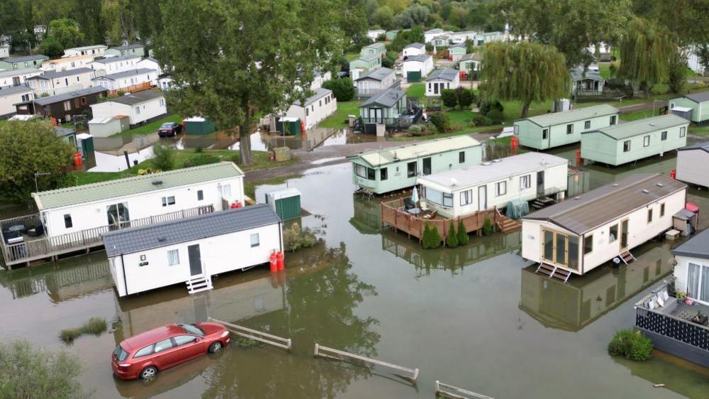 White mobile homes surrounded by water.  A red car is also visible.