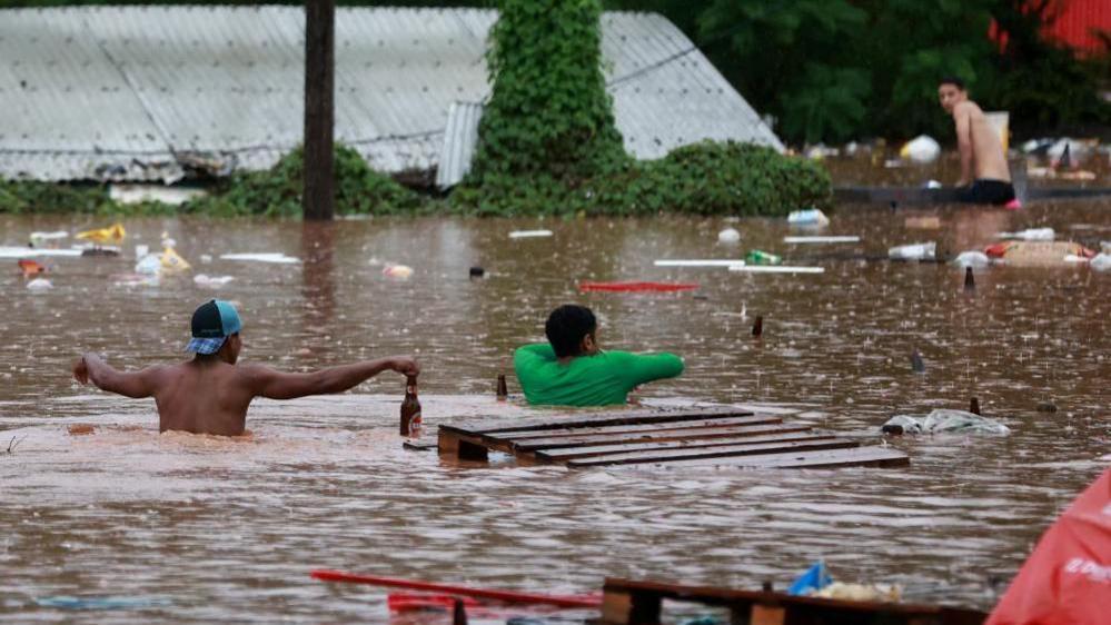 People walk in a flooded area next to the Taquari River during heavy rains in Encantado, Rio Grande do Sul state, Brazil, May 2, 2024.