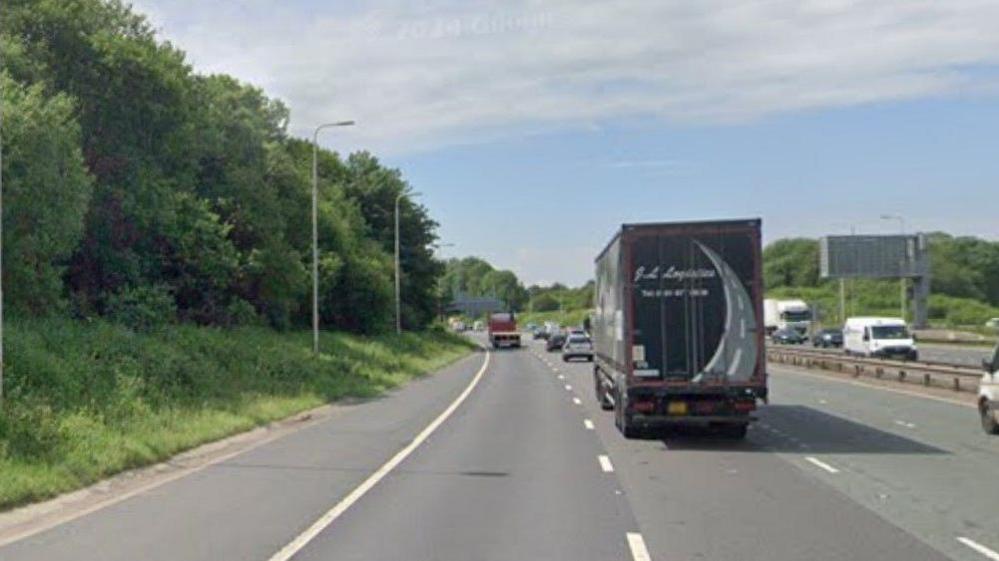 M62 westbound between M602 and junction - lorry in middle lane. Trees on the side of the carriageway.