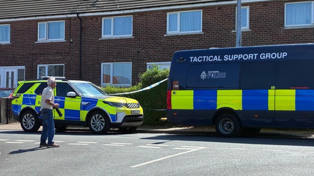Two police vehicles parked outside a cordoned off house in Rotherham