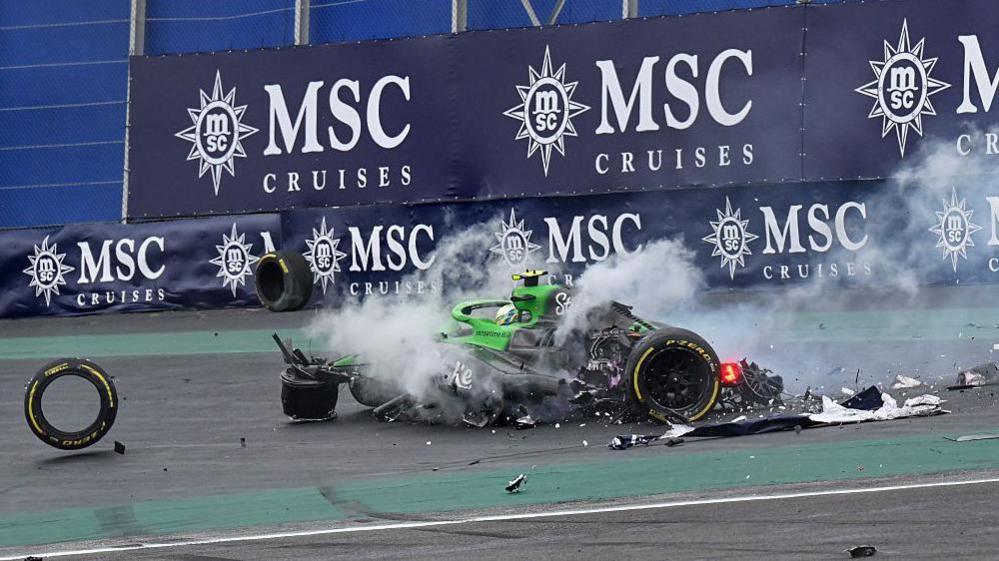 Debris litters the track and smoke rises from the wreckage of Gabriel Bortoleto's Sauber after he crashed as he started the final lap of the sprint