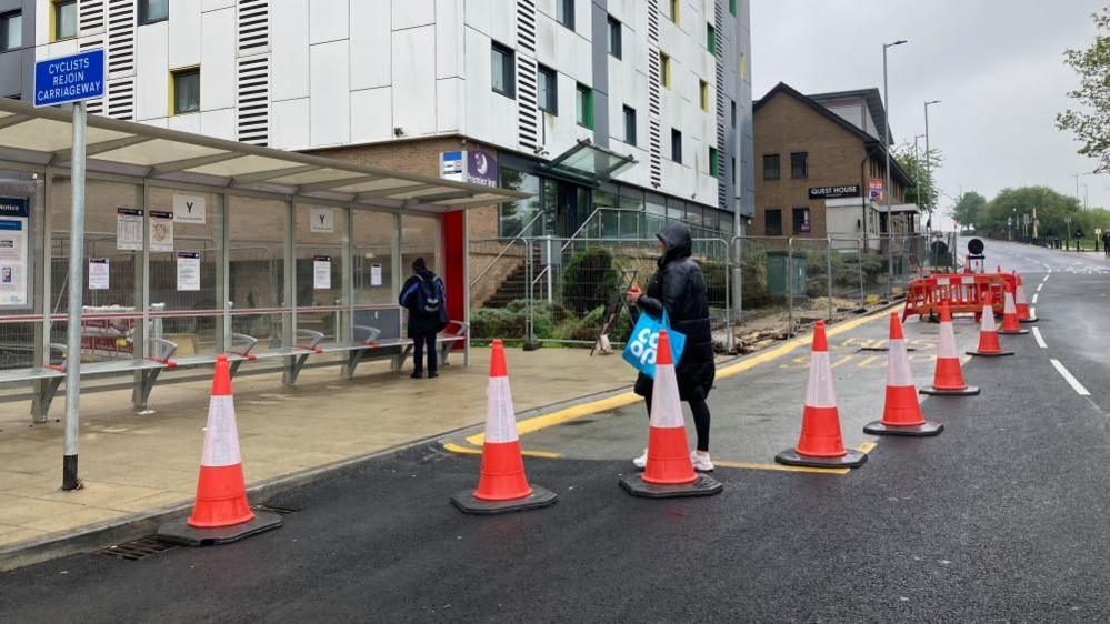 People at a bus stop which is coned off