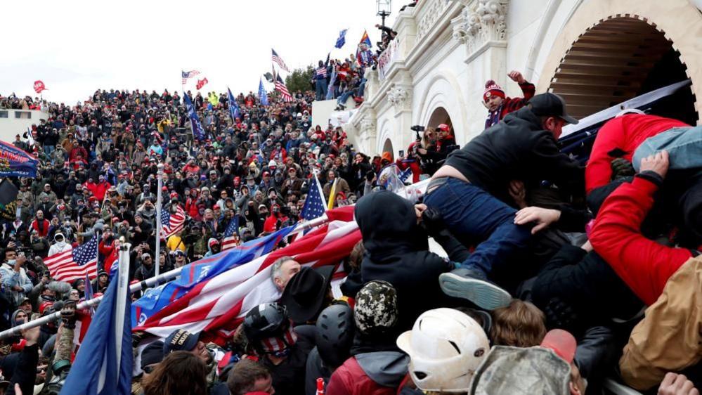 Rioters scale a wall at the US Capitol building