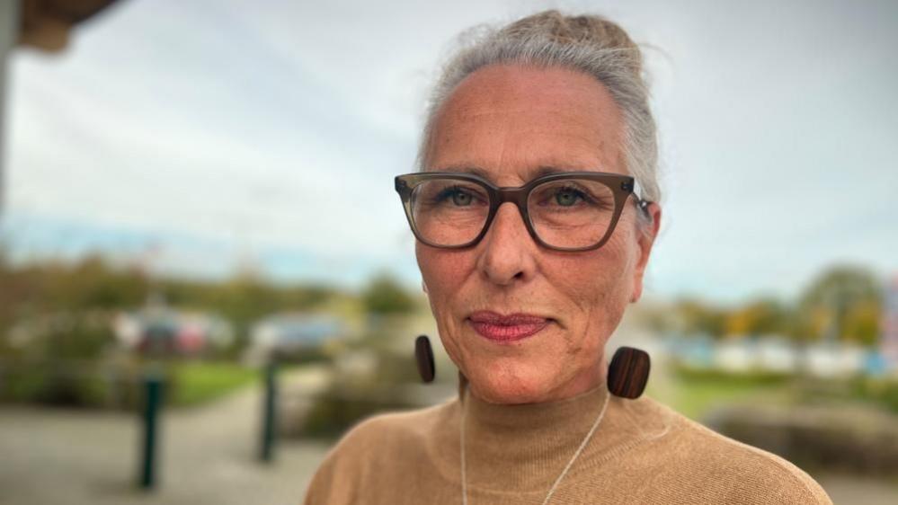 Norah Al-Ani, wearing dark rimmed glasses, her hair tied up, with large earings and a cream top