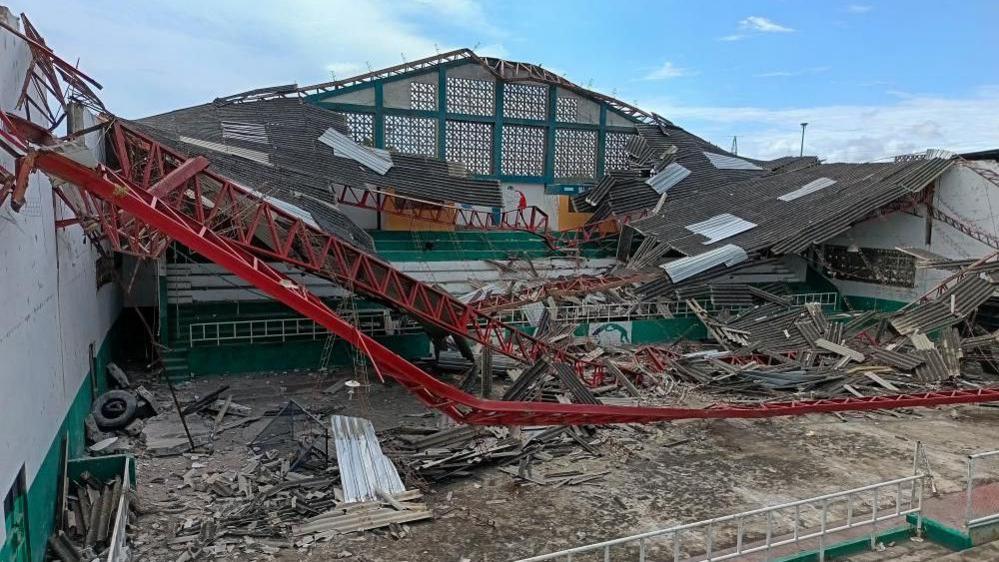 A large building's roof collapsed in on itself with debris and tires inside.