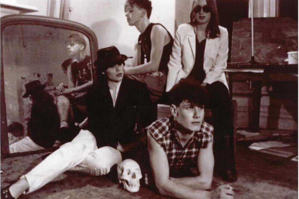 Sir Keir Starmer dressed in a checked shirt with cut-off sleeves props himself up on his arms next to a skull. His friends are posed around him.