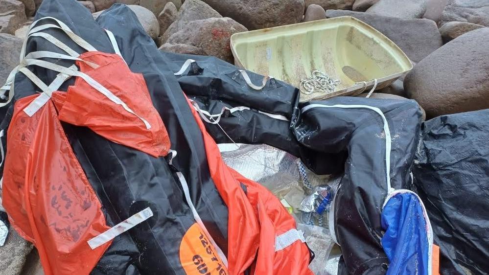 The deflated red and black remains of the life raft, together with its plastic casing, lying on rocks on the beach.