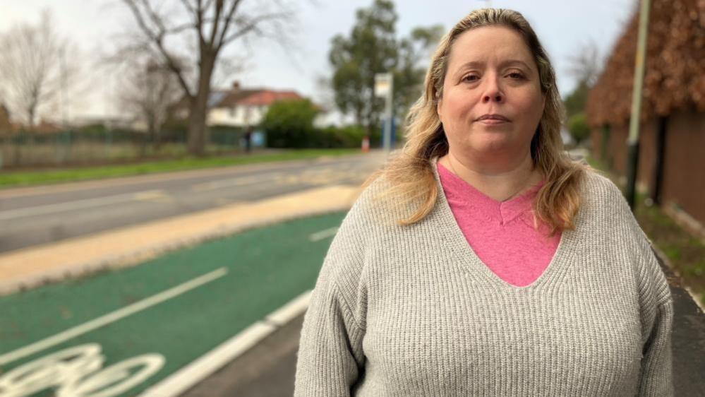 Alice Reeve, wearing a pink and grey top, standing in front of a cycle lane in Cheltenham.