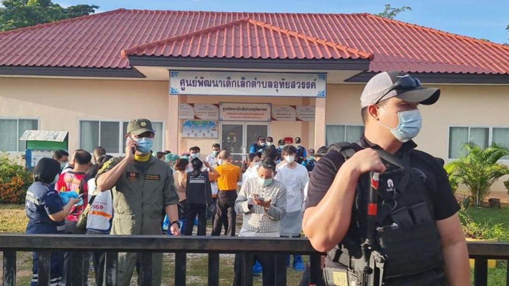 A handout photo made available by Ruamkatanyu Foundation shows an armed police officer standing guard as relatives of the victims of a mass shooting gather at the childcare center