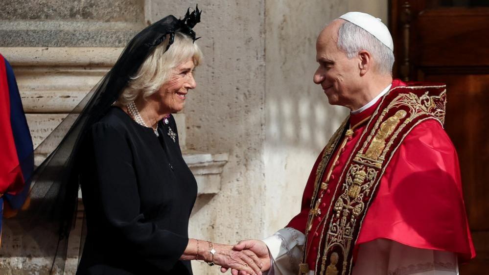 Pope Leo XIV cloaked in red shaking hands with Queen Camilla wearing all black with a black veil
