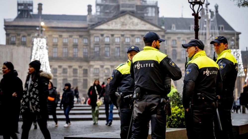 People walk past a police car as officers stand guard on Dam Square in Amsterdam after the violence in the centre of the city the day before