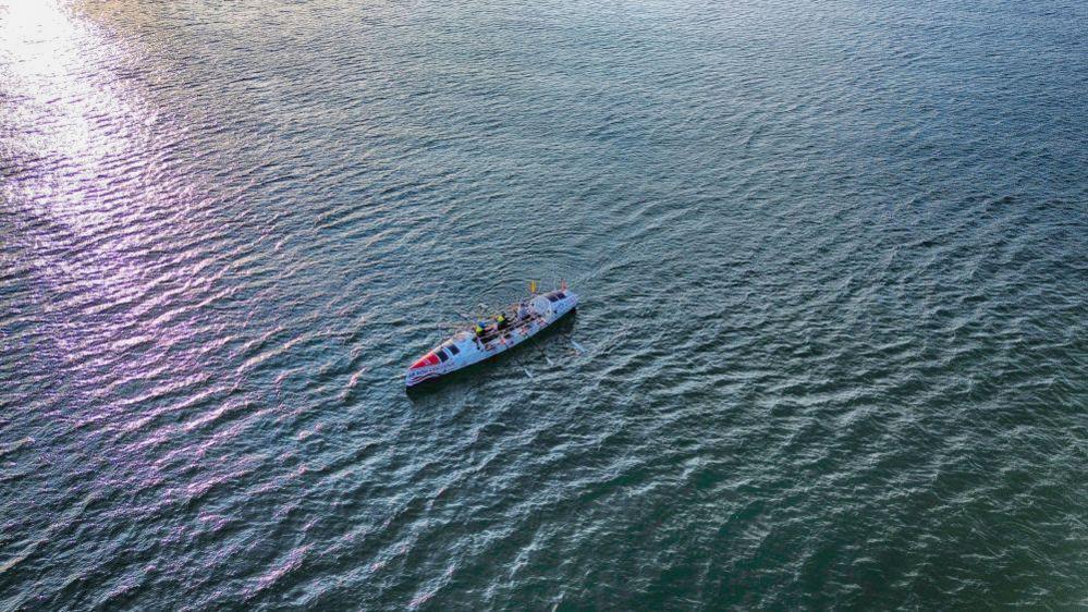 A drone image of a lone rowing boat in the middle of the ocean.