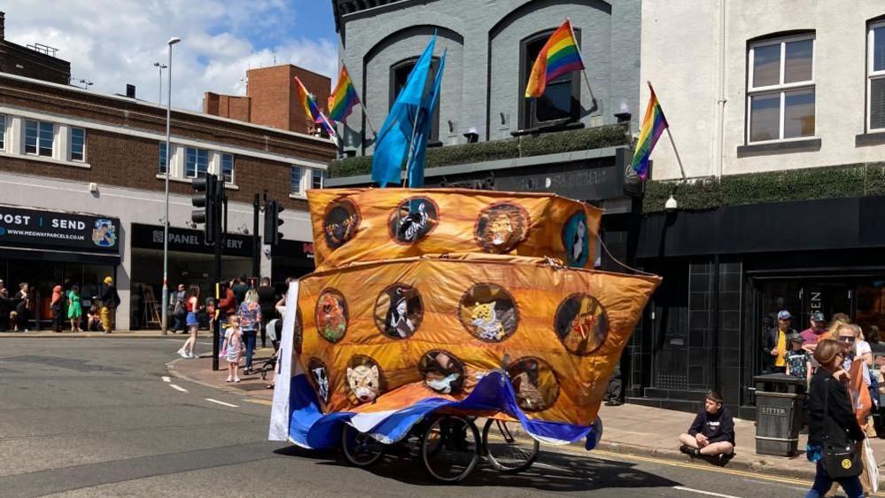 A group of cyclists with a large depiction of Noah's ark covering them 