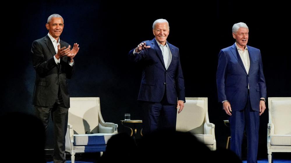 Presidents Obama, Biden and Clinton standing on stage