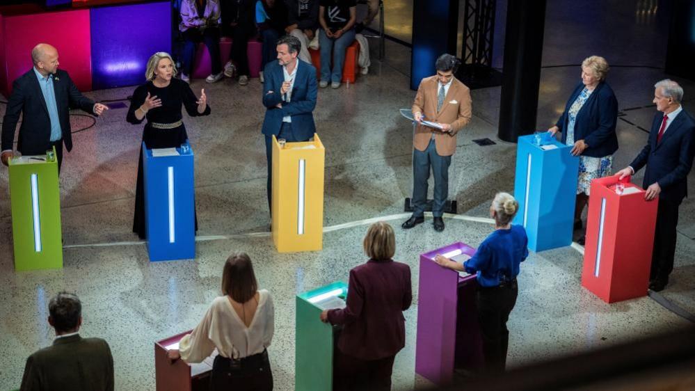 An election debate takes place on 2 September with all the political leaders standing behind lecterns of varying colours