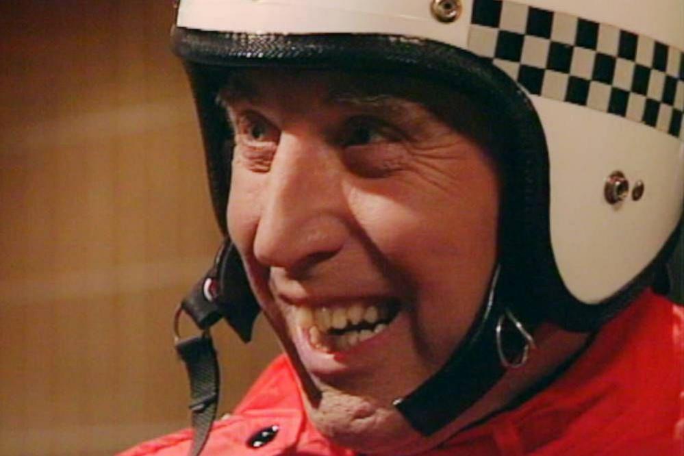 Rikki Fulton in character as supercop. He is wearing a white and black helmet which features a black and white check pattern as well as a red jacket.