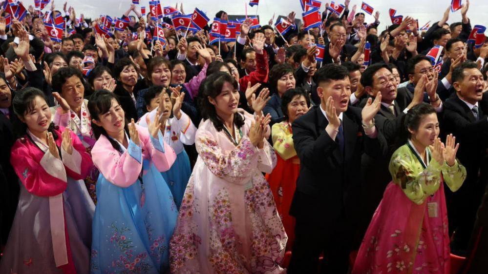 Performers dressed in colourful traditional costumes clap and raise North Korean flags during the event