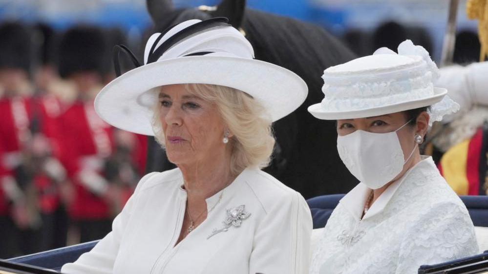 Britain's Queen Camilla and Japan's Empress Masako, wearing a mask, ride in an open carriage