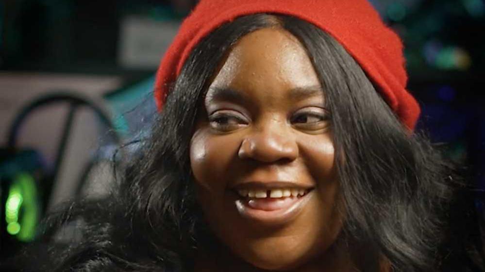 A woman with long black hair and wearing a red hat smiles while looking away from the camera