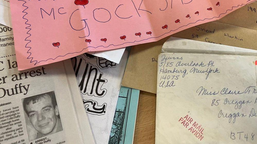 A wide range of letters, newspaper cuttings and magazines are sprad across a wooden table