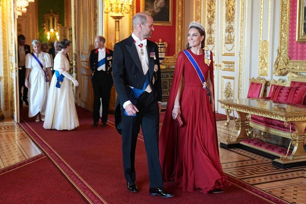 The Prince and Princess of Wales smile at each other as they walk to the banquet hall in Windsor Castle. Other senior royals are chatting behind them as they walk through a door.